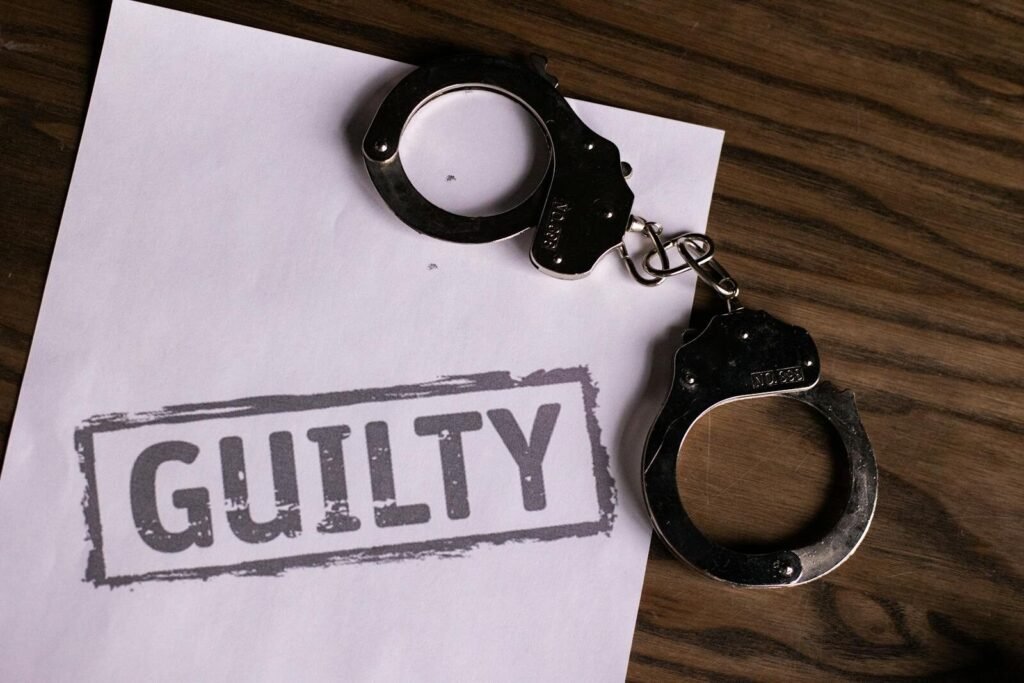 Top view of handcuffs on paper with 'GUILTY' text, symbolizing a verdict or crime.